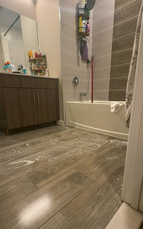 Small bathroom with vanity, tub, towel ladder, and wood-look tile floor.