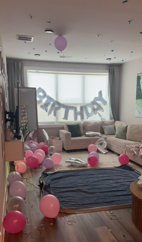 Birthday-decorated living room with balloons, banner, and a gift box on the floor.