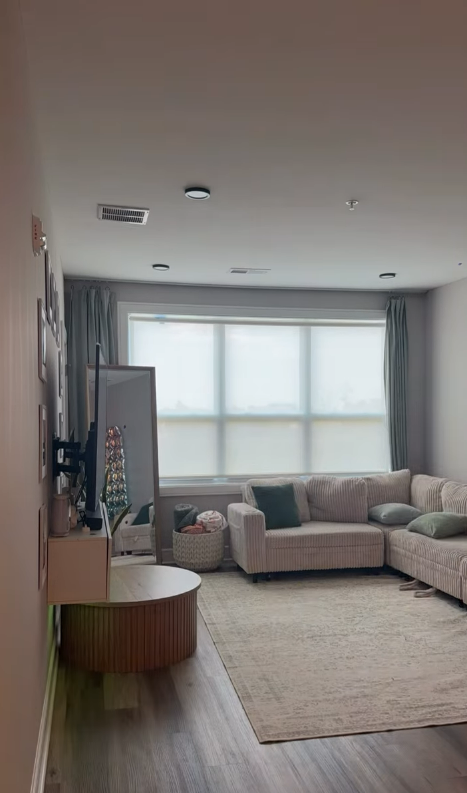 Bright living room with a gray sectional, beige rug, curtains, and large window