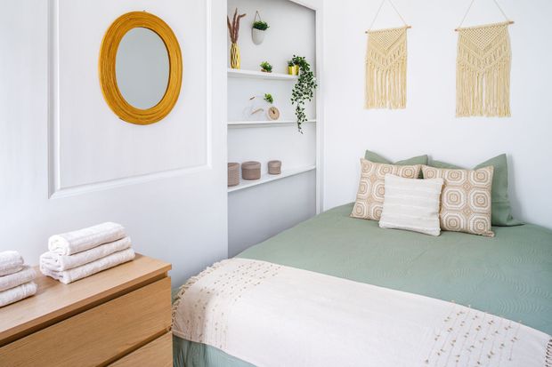 Bright bedroom with mint bedspread, woven wall decor, white shelves, and a wooden dresser