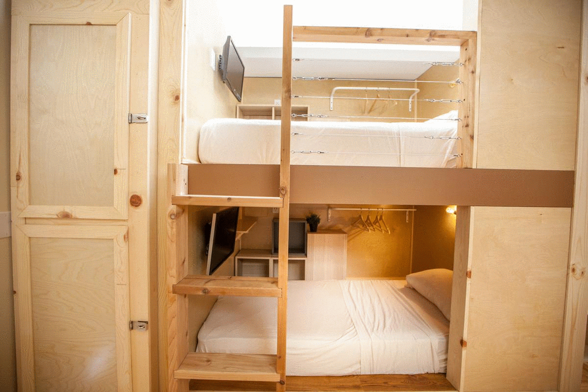 Bunk bed unit made of wood, with beds stacked and small TVs, in a small room.