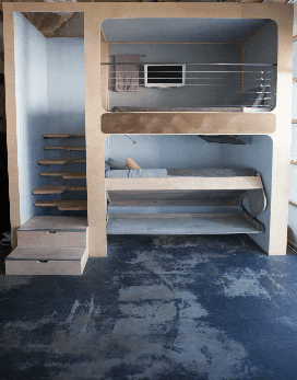 A two-story bunk bed with a wooden frame and stairs. The lower bunk is occupied by someone lying down.
