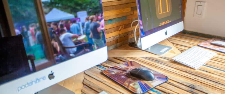 Two desktop computers on a wooden desk, one showing a crowd outside and one displaying a yellow icon