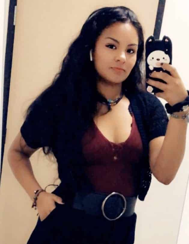 Woman taking a mirror selfie in a black outfit with a burgundy top and large belt.