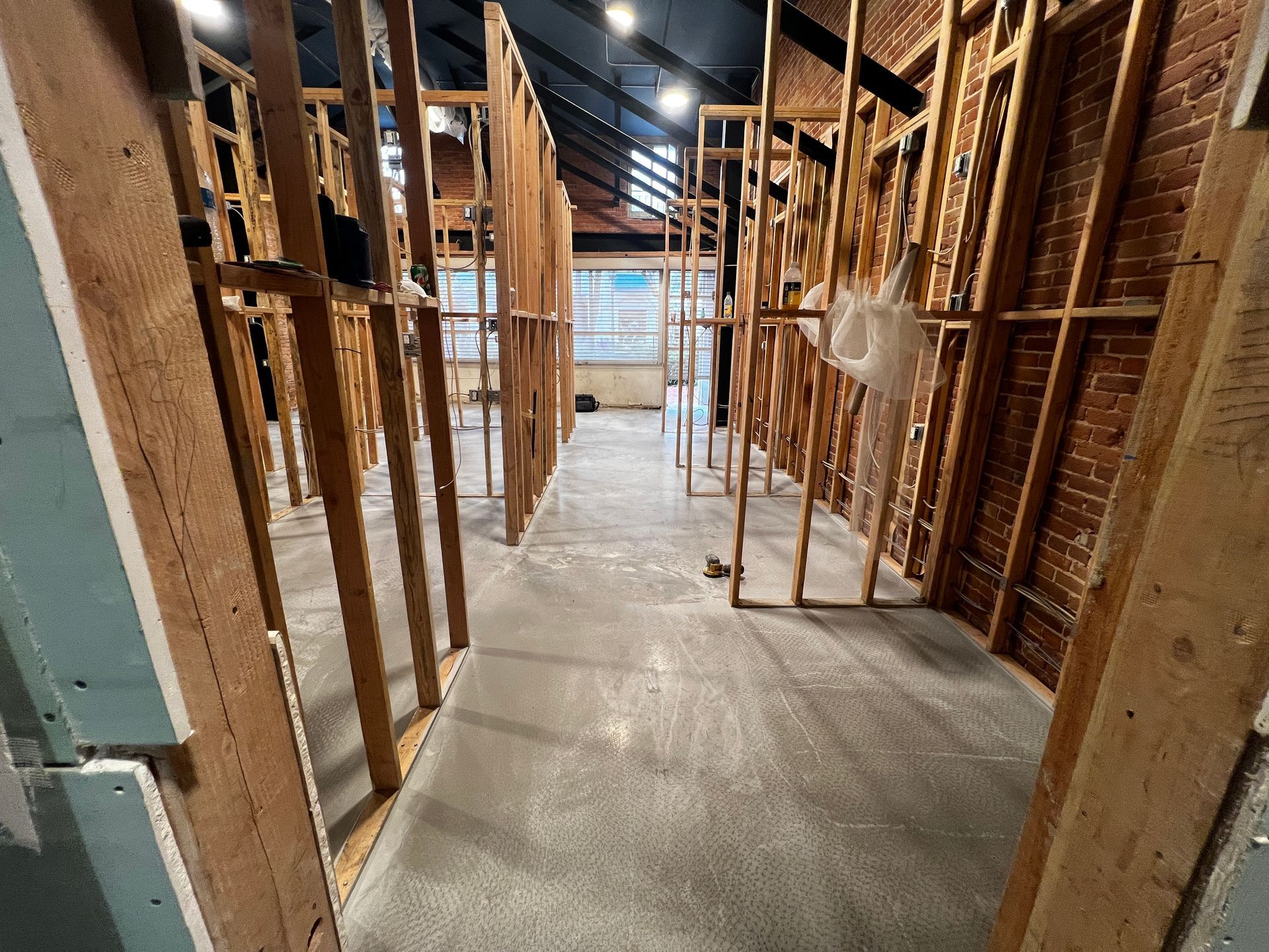 Construction-framed hallway with exposed wooden studs and a concrete floor inside an unfinished building