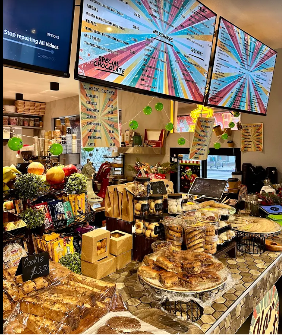 Bakery counter with assorted pastries, cakes, and colorful menu boards overhead