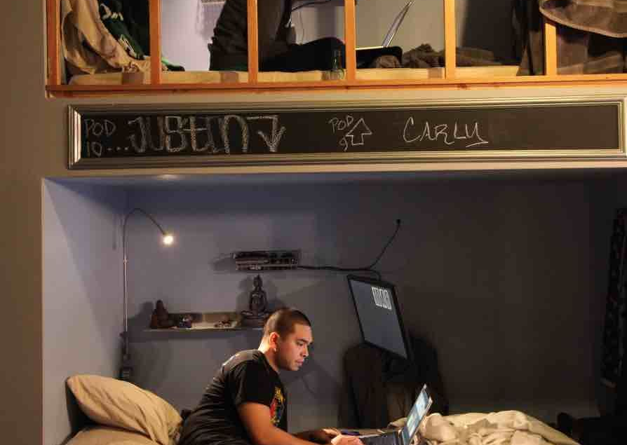 Two stacked loft beds in a small room, with people sitting on the lower bed and upper loft.