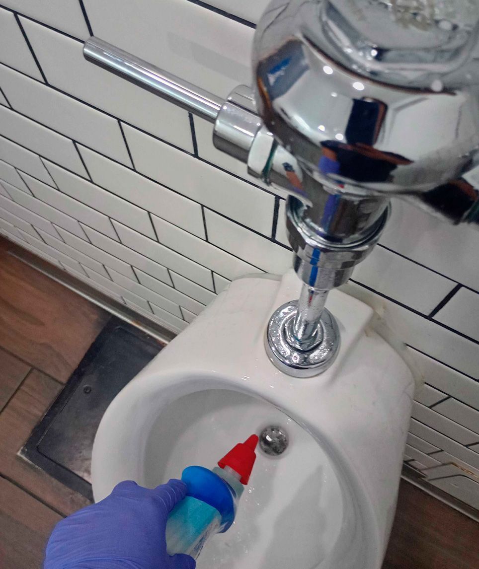 Handwashing sink with a chrome flush valve and a gloved hand cleaning the basin with a red brush