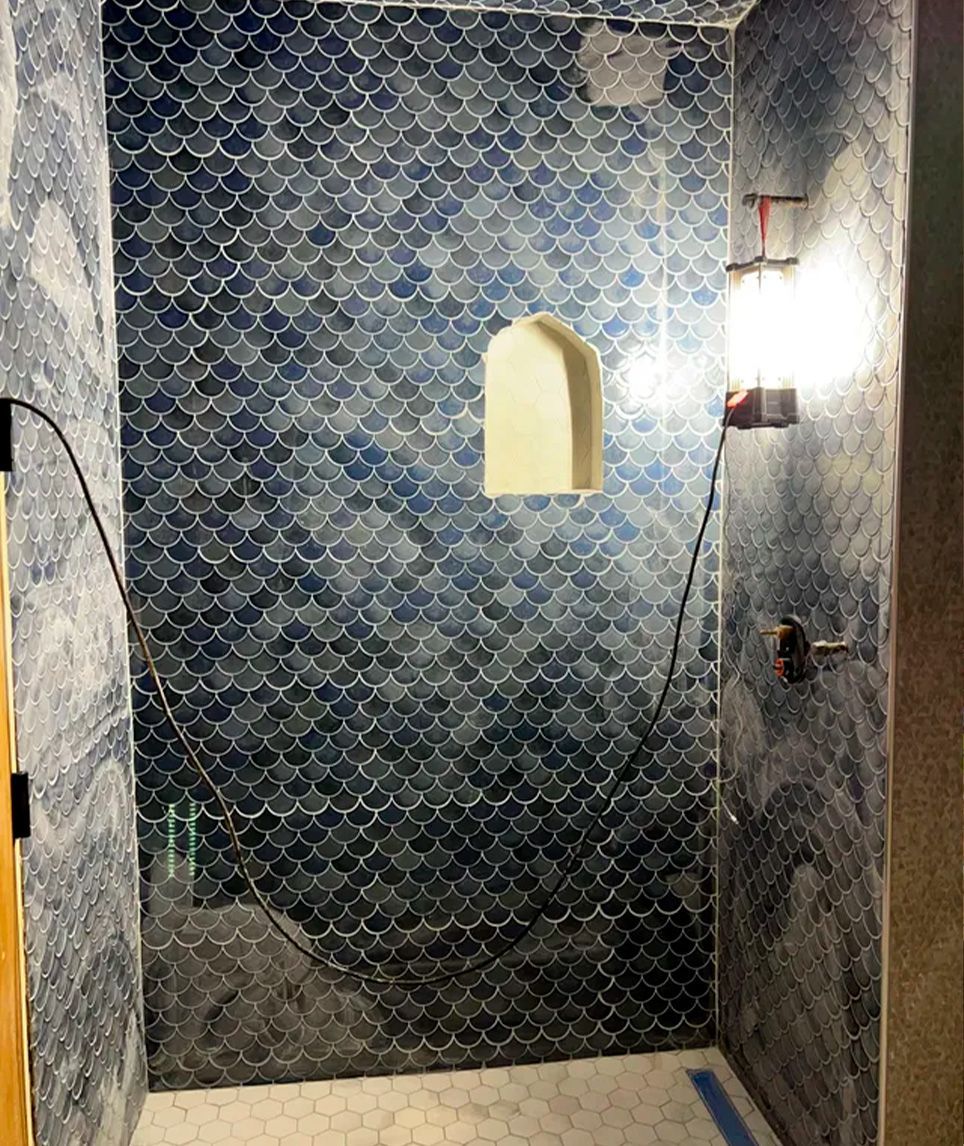 Blue tiled shower alcove with a small arched niche and a wall light on the right side.