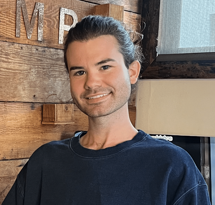Person smiling in a navy shirt against a rustic wooden wall.