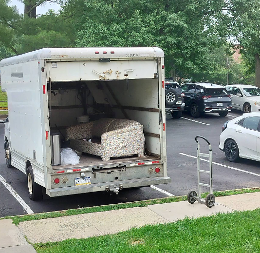 Moving truck parked in a parking lot, furniture inside, hand truck on the curb.