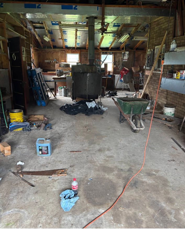 Cluttered workshop interior; concrete floor, large central furnace, tools, and materials strewn about.