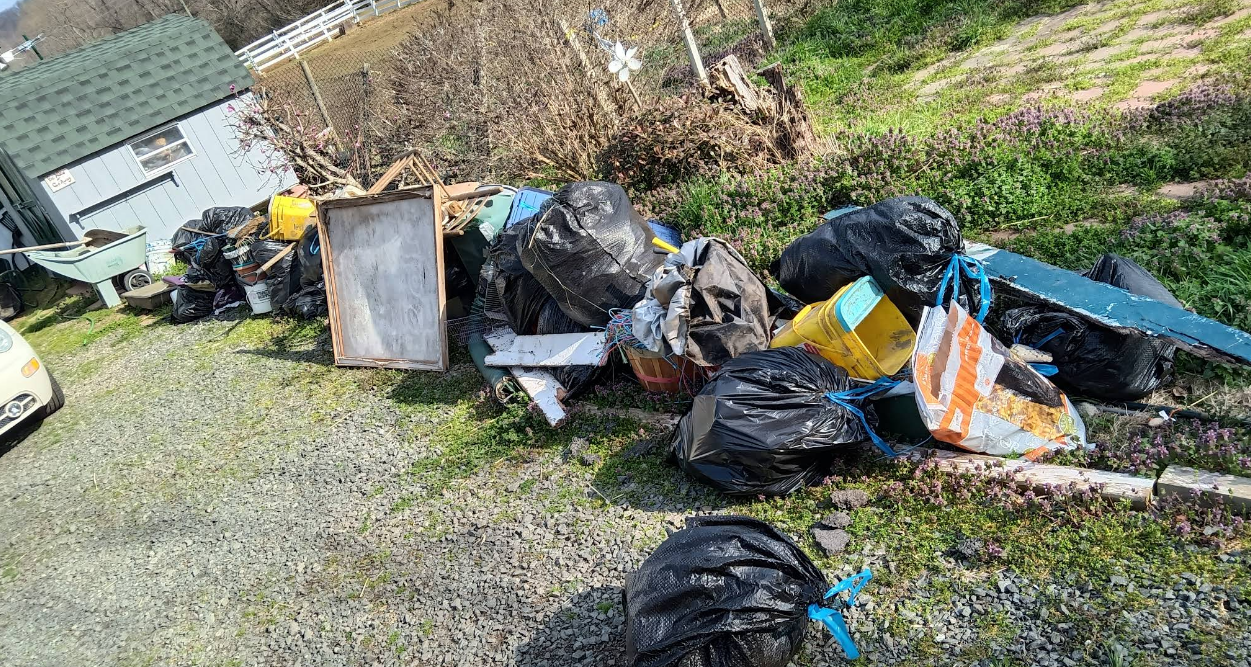 Pile of trash bags, wooden frame, and debris strewn on grass next to a building.