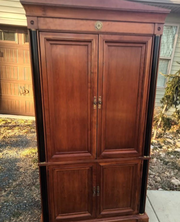 Dark wood armoire with black trim; standing outside.