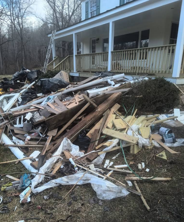Pile of construction debris in front of a house with a porch. Includes wood, plastic, and other trash.