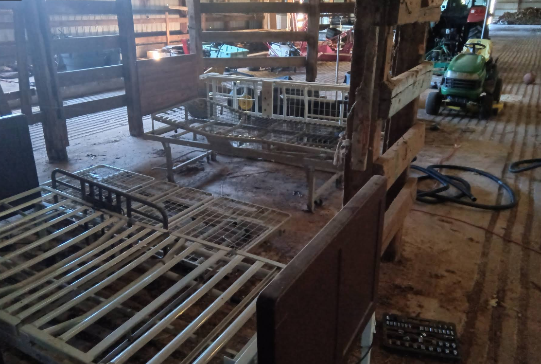 Several metal bed frames disassembled in a barn; a tractor sits nearby.