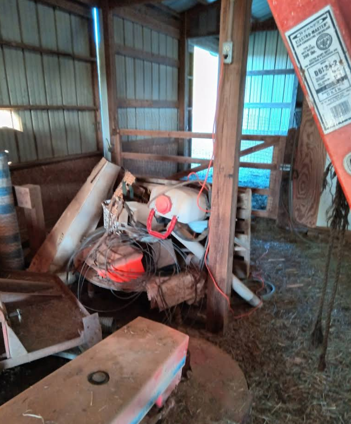 Cluttered barn interior with a pile of debris, including metal and wood; bright light at the back.