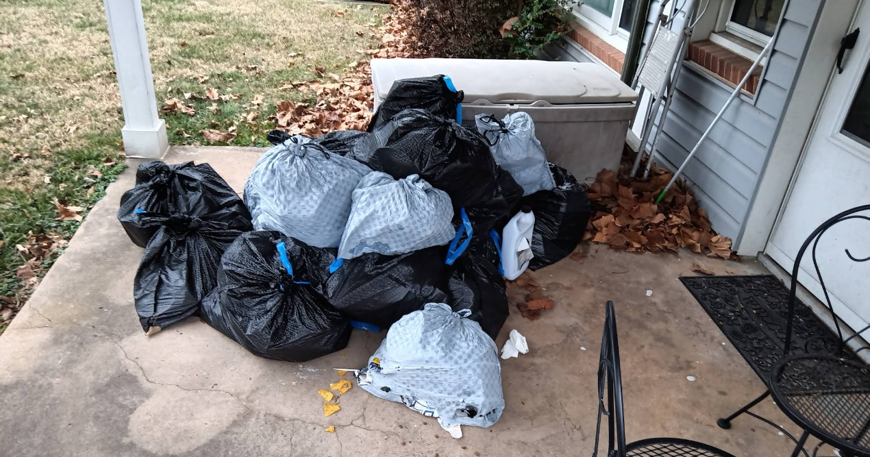 A pile of black and gray trash bags on a porch, likely waiting for pickup.