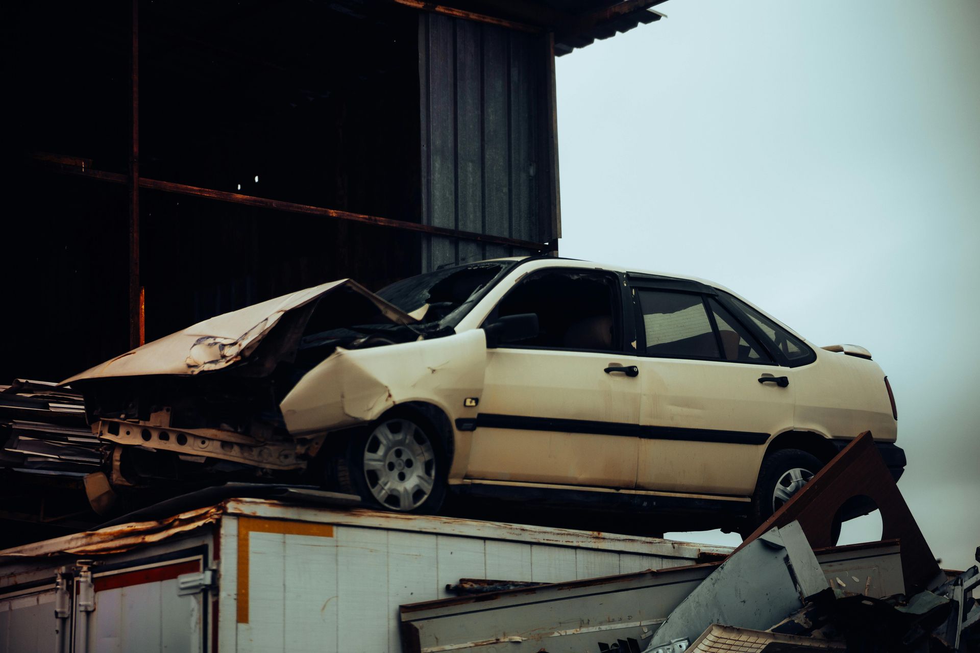 Damaged white car on a pile of debris, next to a weathered building.