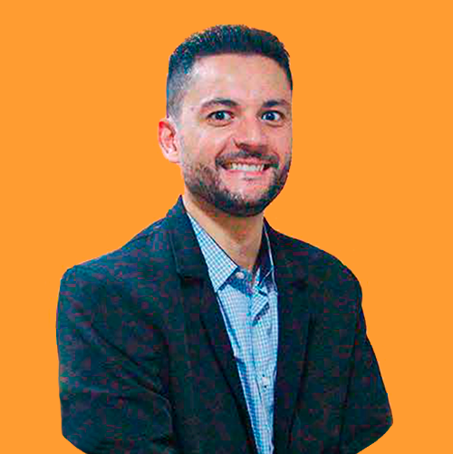 Um homem com barba está vestindo terno e sorrindo.