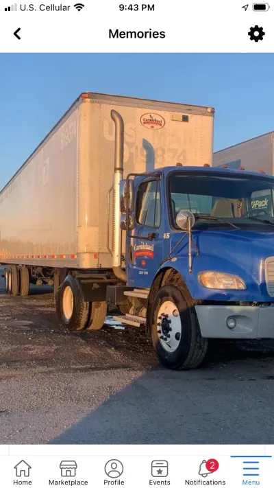 Blue semi truck hauling a white trailer parked in a lot at sunset