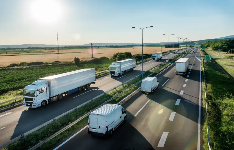 Several trucks drive along a highway beside a dry, open landscape at sunset.
