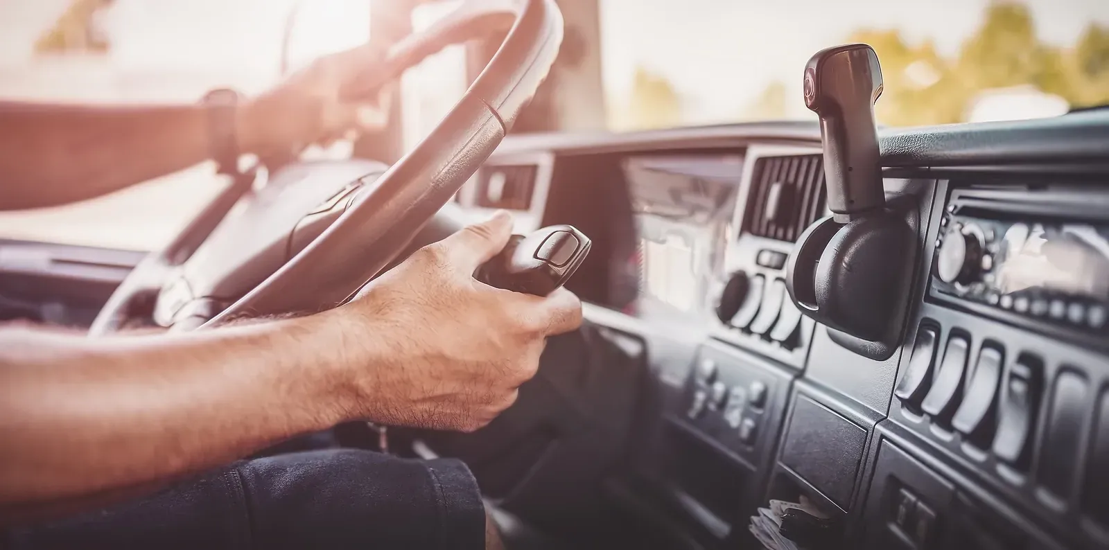 Driver’s hands on steering wheel inside a vehicle, with dashboard and gear shift visible.