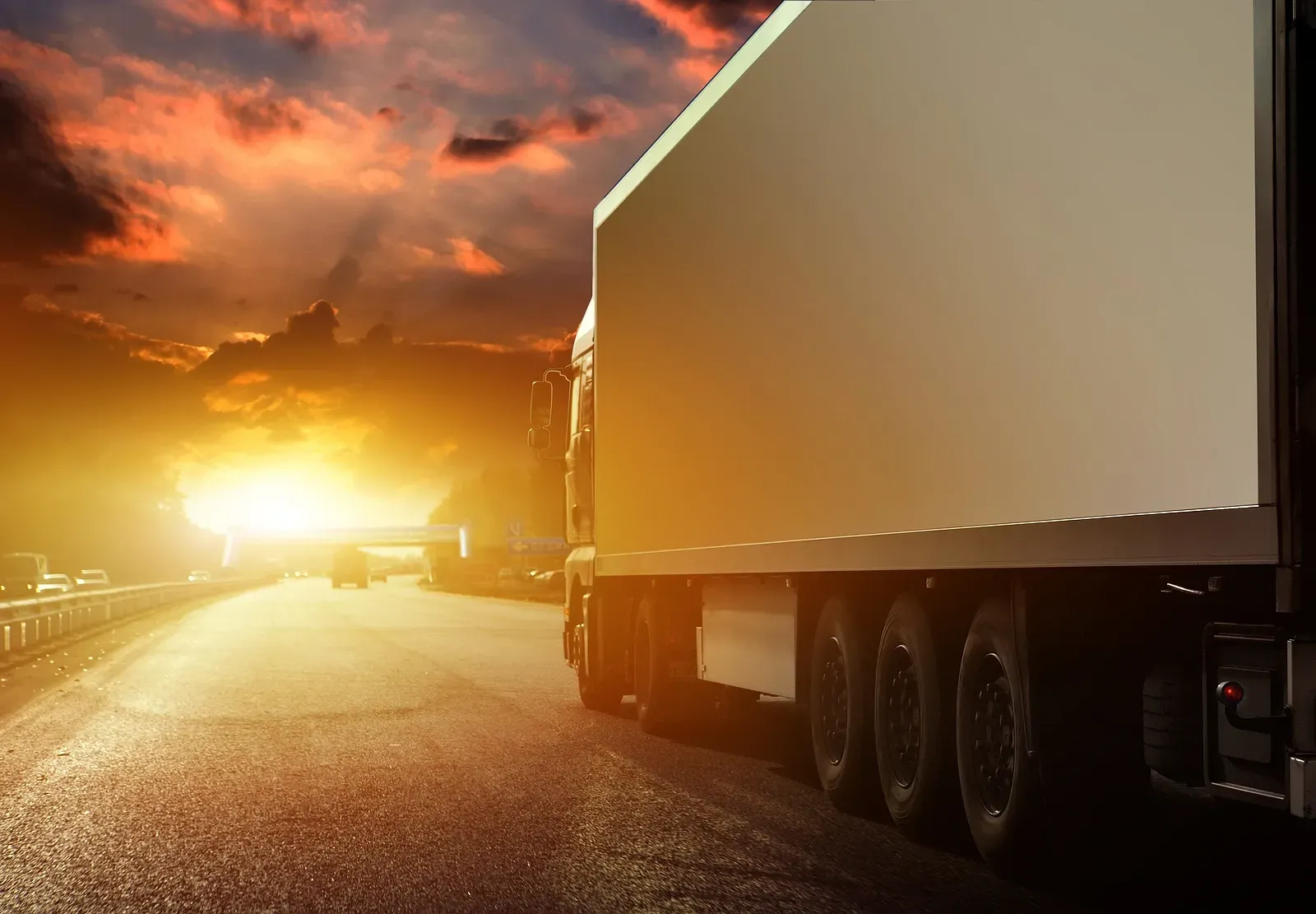 Semi-trailer truck on a road at sunset with bright headlights and orange sky