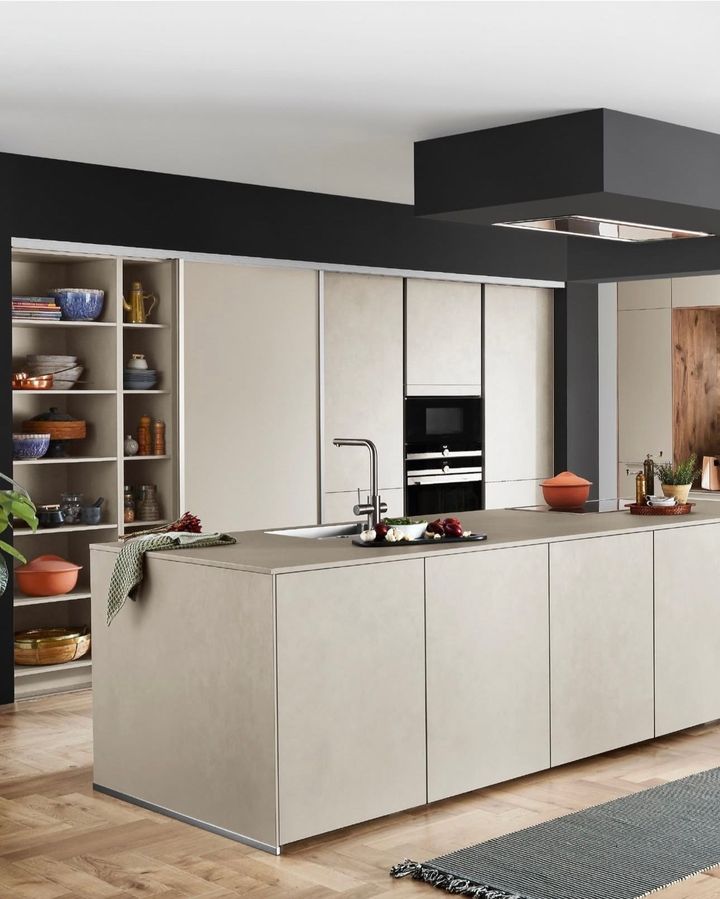 Modern beige kitchen with dark walls, island, built-in appliances, and open shelving with various items.