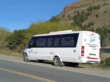 Minibús blanco con logotipo azul en una carretera, montaña al fondo.