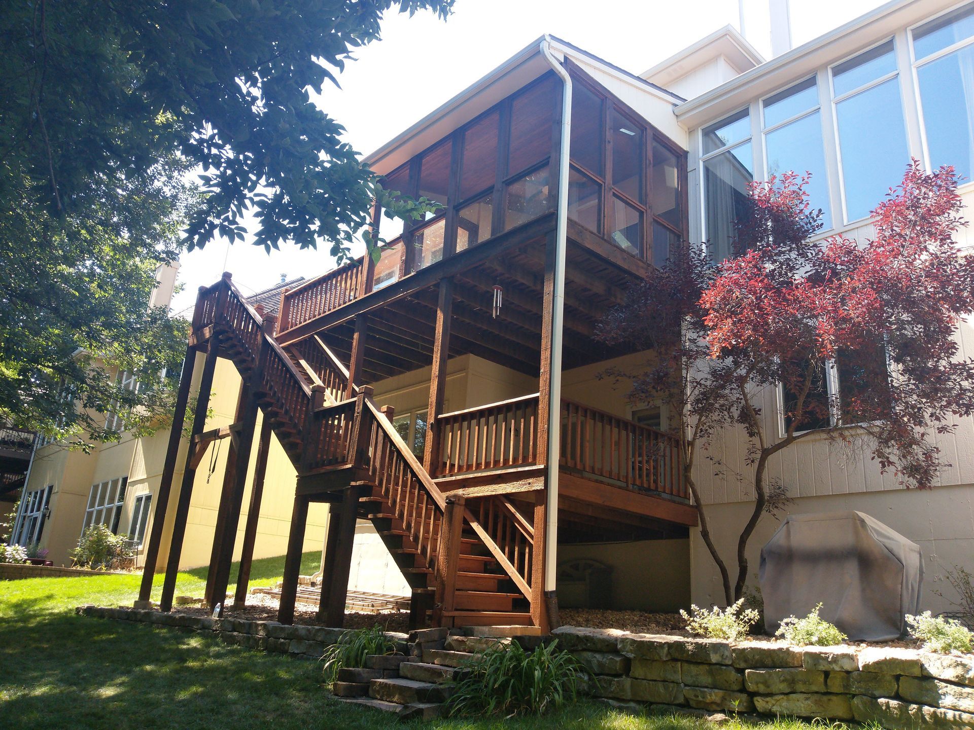 Wooden deck with stairs, built against a house. A screened-in porch is at the top level.
