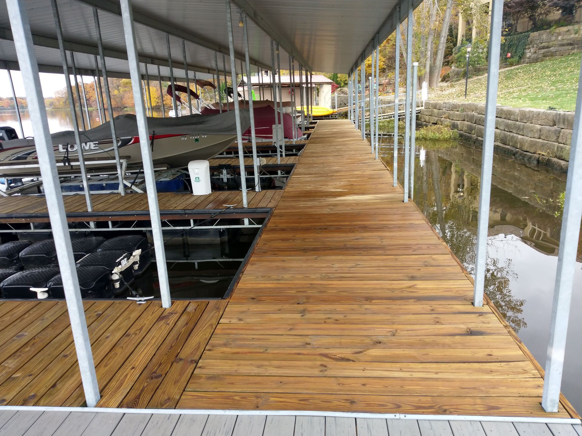 Wooden dock extending over water, under a covered walkway with boats docked on the left.
