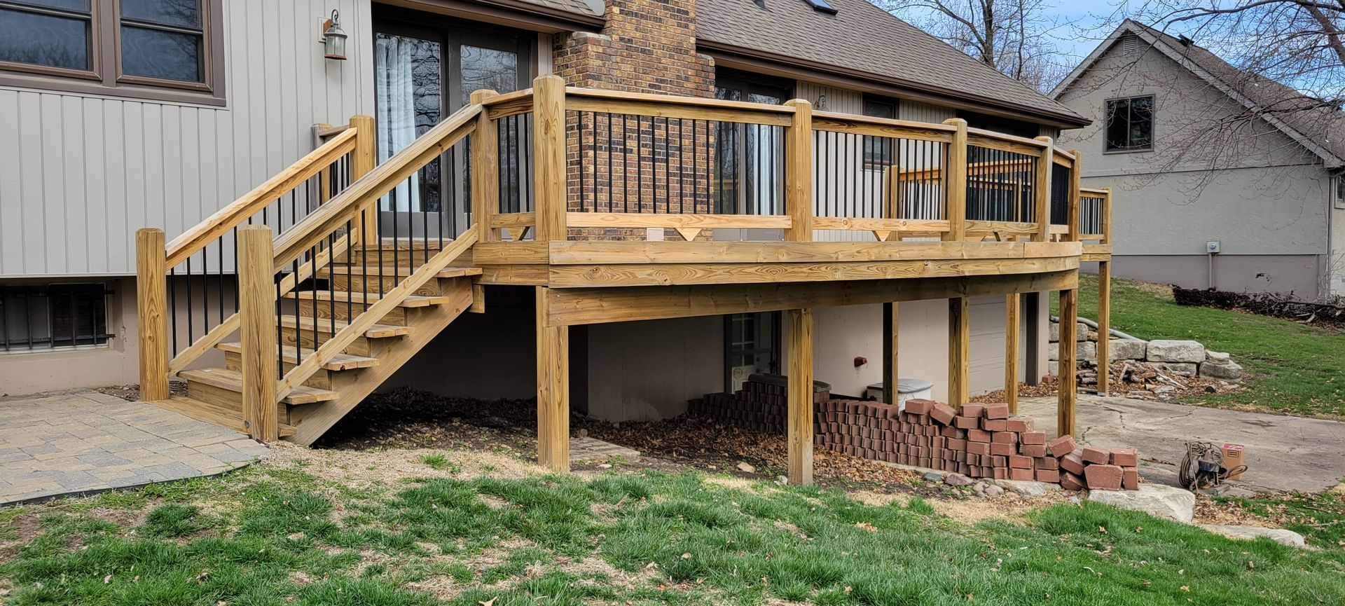 Wooden deck with stairs attached to a beige house, next to a grassy yard.
