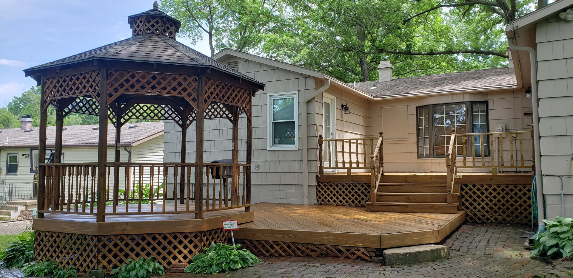 A backyard with a wooden gazebo and deck attached to a light-colored house.