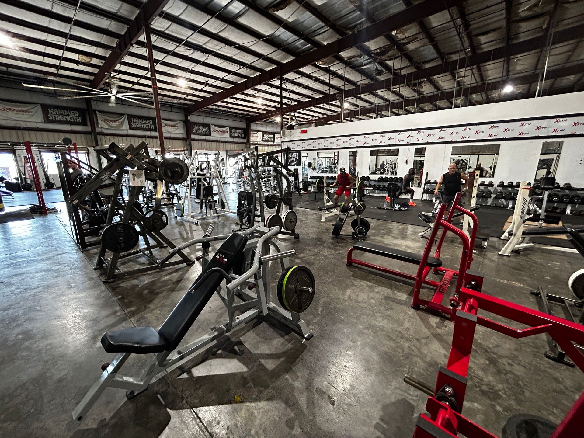 Gym interior with weight machines, free weights, and people working out.