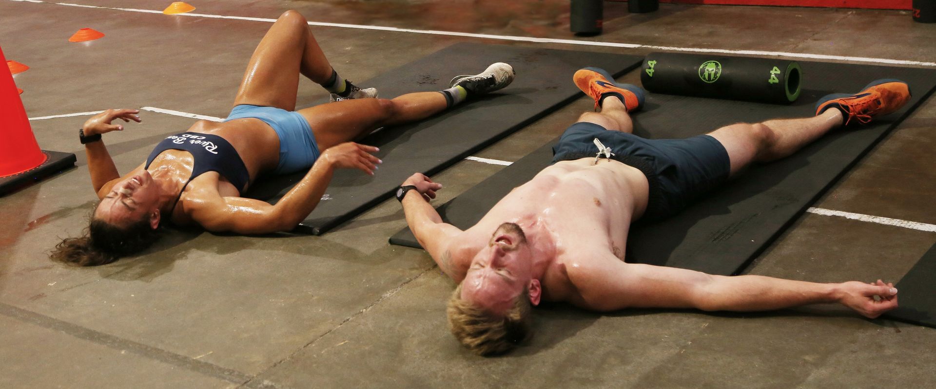Two sweaty people lie on mats, arms outstretched, after a workout.