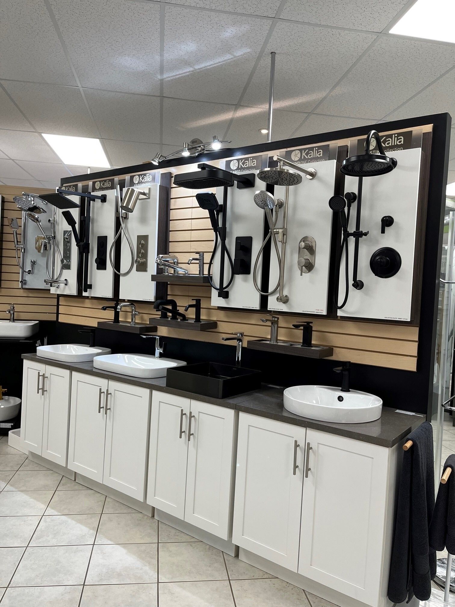 Espace de lavage de cheveux avec trois miroirs, sèche-cheveux, lavabos et armoires blanches le long d'un mur carrelé.