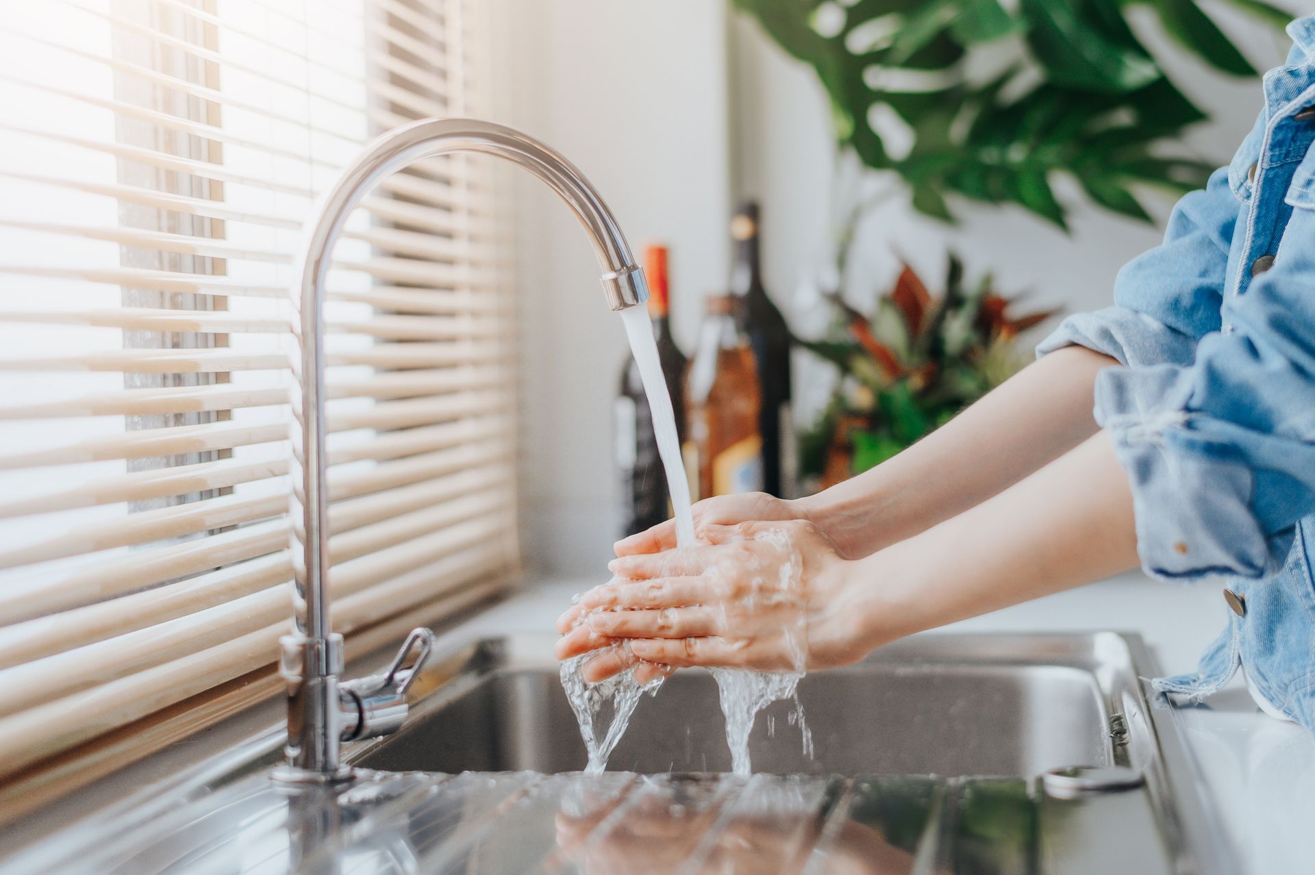 Une personne se lave les mains dans un évier en acier inoxydable, l'eau coule.