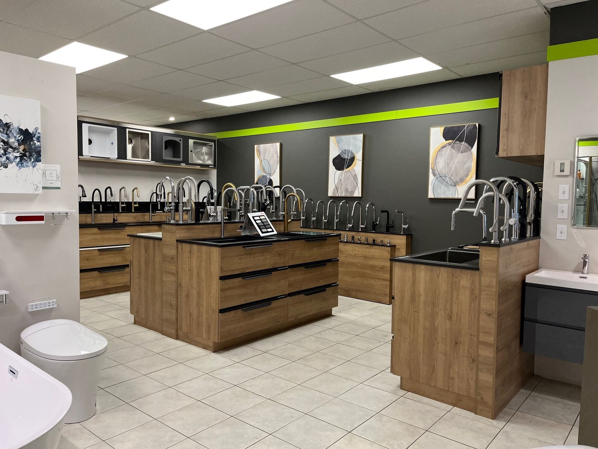 Salle d'exposition de cuisines modernes avec îlots de cuisine en bois, éviers noirs et éclairage zénithal lumineux.