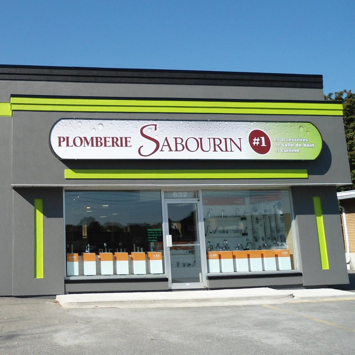 Devanture de magasin Plomberie Sabourin avec extérieur gris, accents verts et fournitures de plomberie en vitrine.