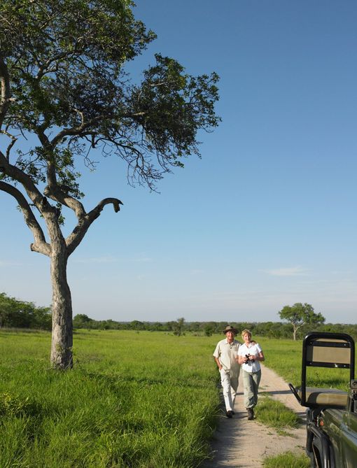 Two people are walking down a dirt path next to a jeep.