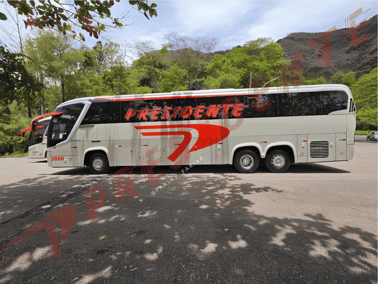 Ônibus de turismo branco com detalhes em vermelho estacionado em uma estrada arborizada na montanha, próximo a uma curva.