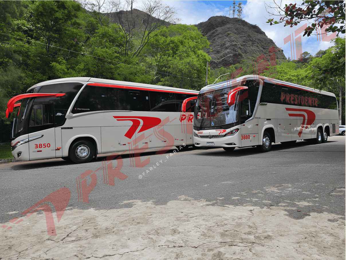 Dois ônibus turísticos brancos estacionados em uma estrada de montanha sob um céu nublado, com detalhes e logotipos em vermelho.