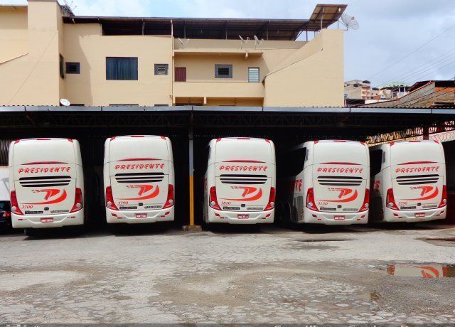 Cinco vans de entrega brancas estacionadas em um estacionamento coberto em frente a um prédio bege.