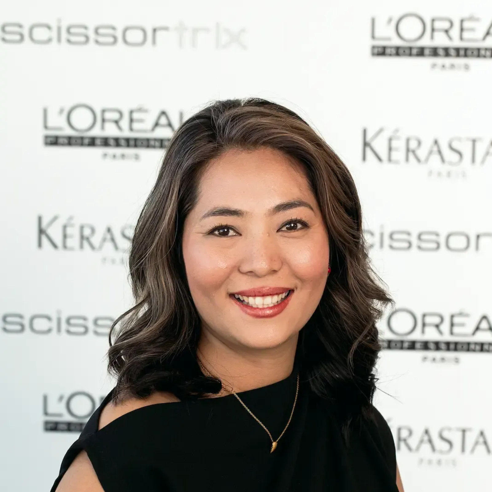 A woman with long hair is smiling in front of a loreal sign.
