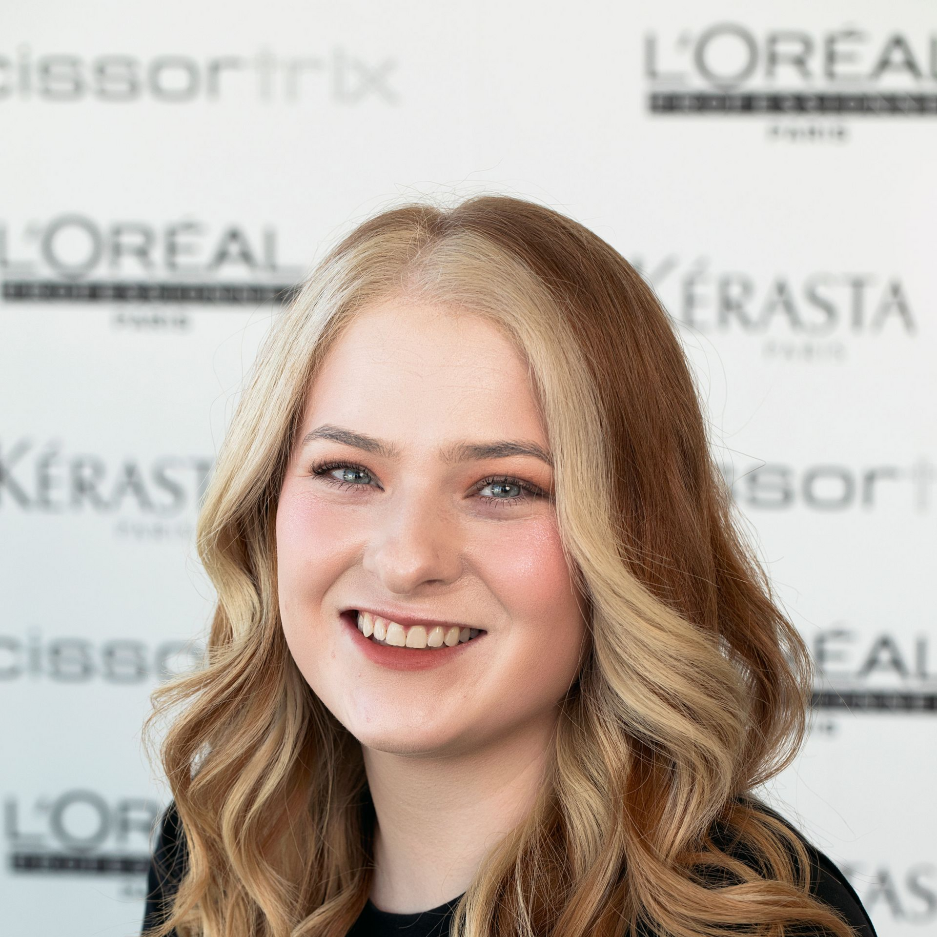A woman with long hair is smiling in front of a loreal sign.