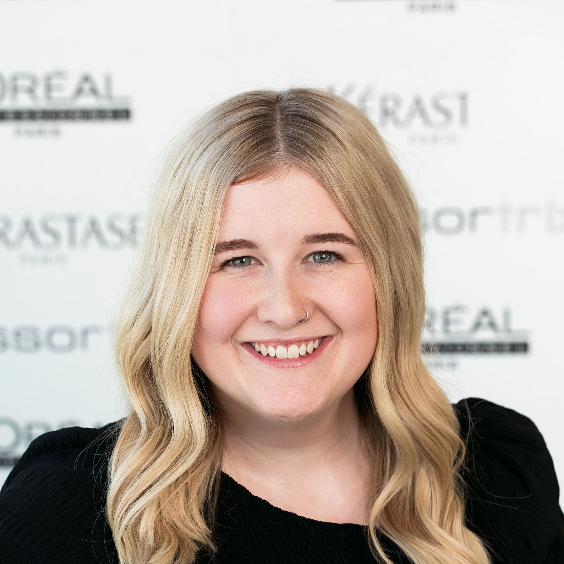 A woman with blonde hair is smiling and wearing a black shirt.