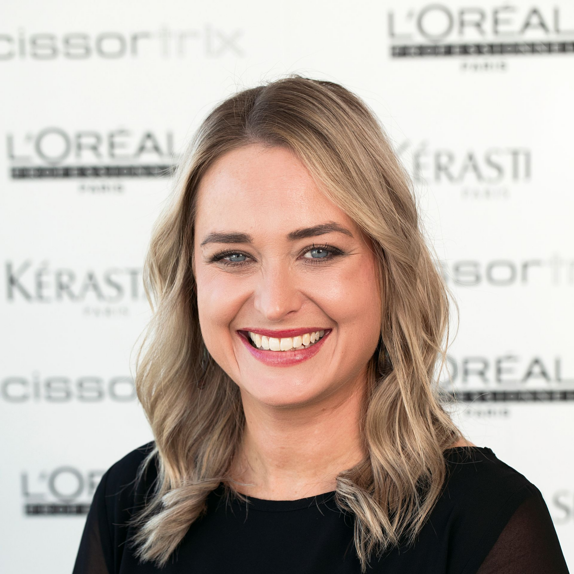 A woman with blonde hair is smiling and wearing a black shirt