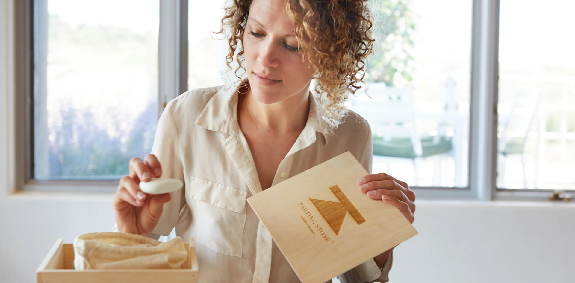 Woman packing a labeled gift box at a table near a window
