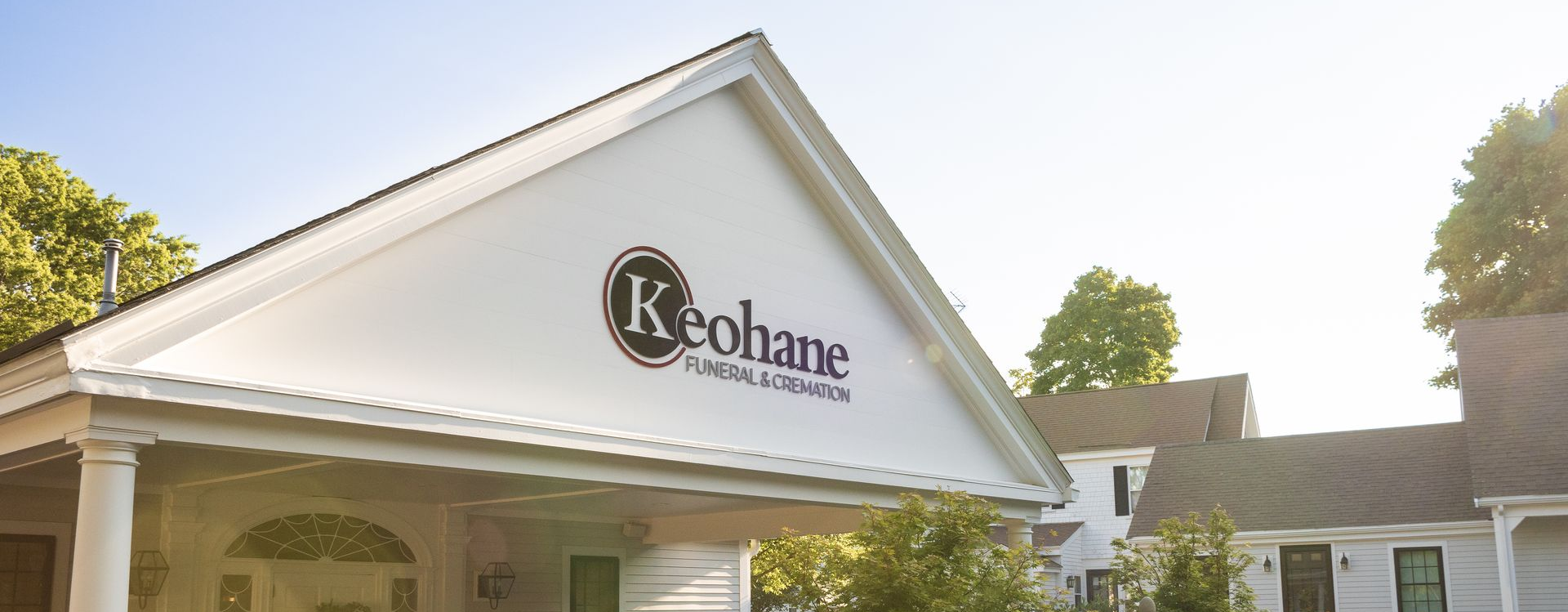 White building with a peaked roof and Keelane sign, sunlit exterior